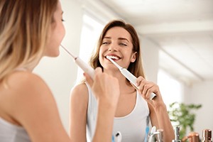 Woman smiling and brushing her teeth in mirror