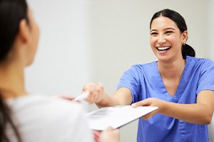 Woman in blue scrubs accepting paperwork from patient