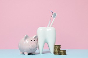 Piggy bank next to model tooth and pile of coins with pink background