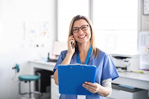 dental assistant smiling while talking on phone and holding blue clipboard