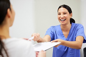 Dental assistant smiling while handing patient form