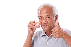 Older man giving thumbs up while holding dentures