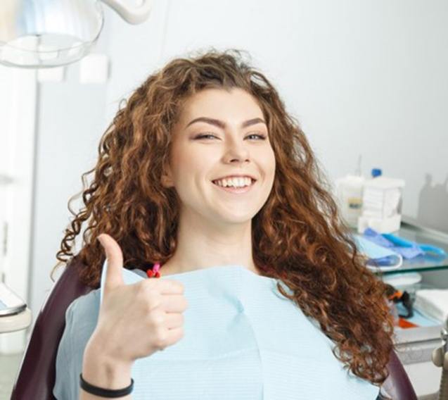 Smiling young woman giving thumbs up in dentist’s chair 