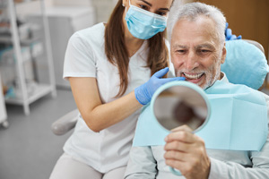 Man smiling at reflection in handheld mirror with dentist
