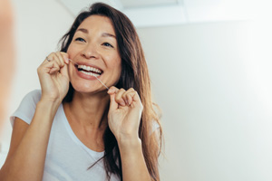 Woman smiling while flossing her teeth in bathroom