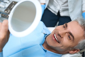 Man with veneers smiling at reflection in dental mirror