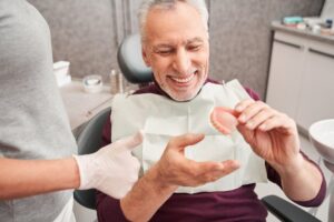 Man handing his ill-fitting dentures to his dentist